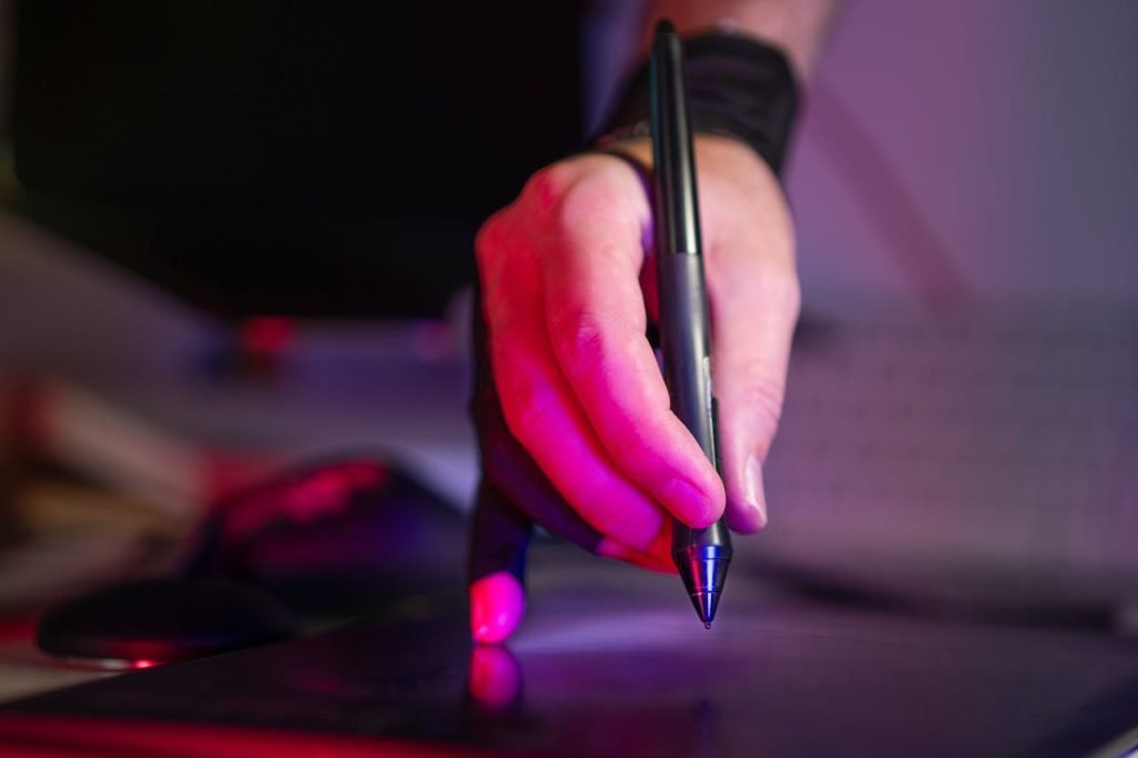 A digital artists hand working on a graphics tablet with a stylus, in a creative studio setting.